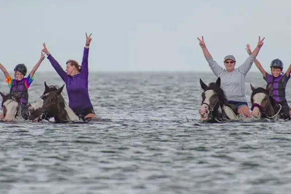 a group of people riding horses in the water